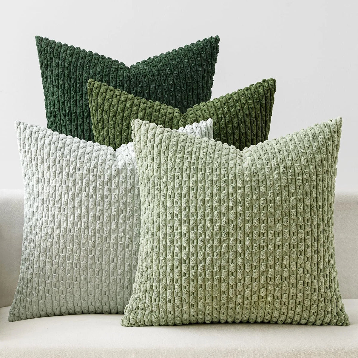 Collection of textured corduroy pillow covers in green shades arranged on a couch