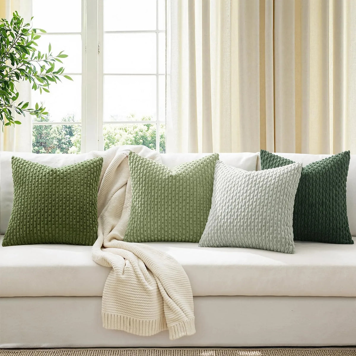 Couch with five green corduroy pillow covers and cream throw blanket by a window