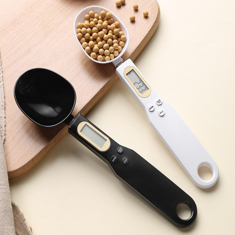 Black and white digital measuring spoons with LCD screens on a light wooden board