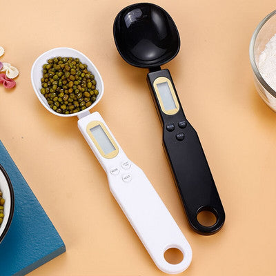 Two digital measuring spoons with green beans and black beans on a beige surface